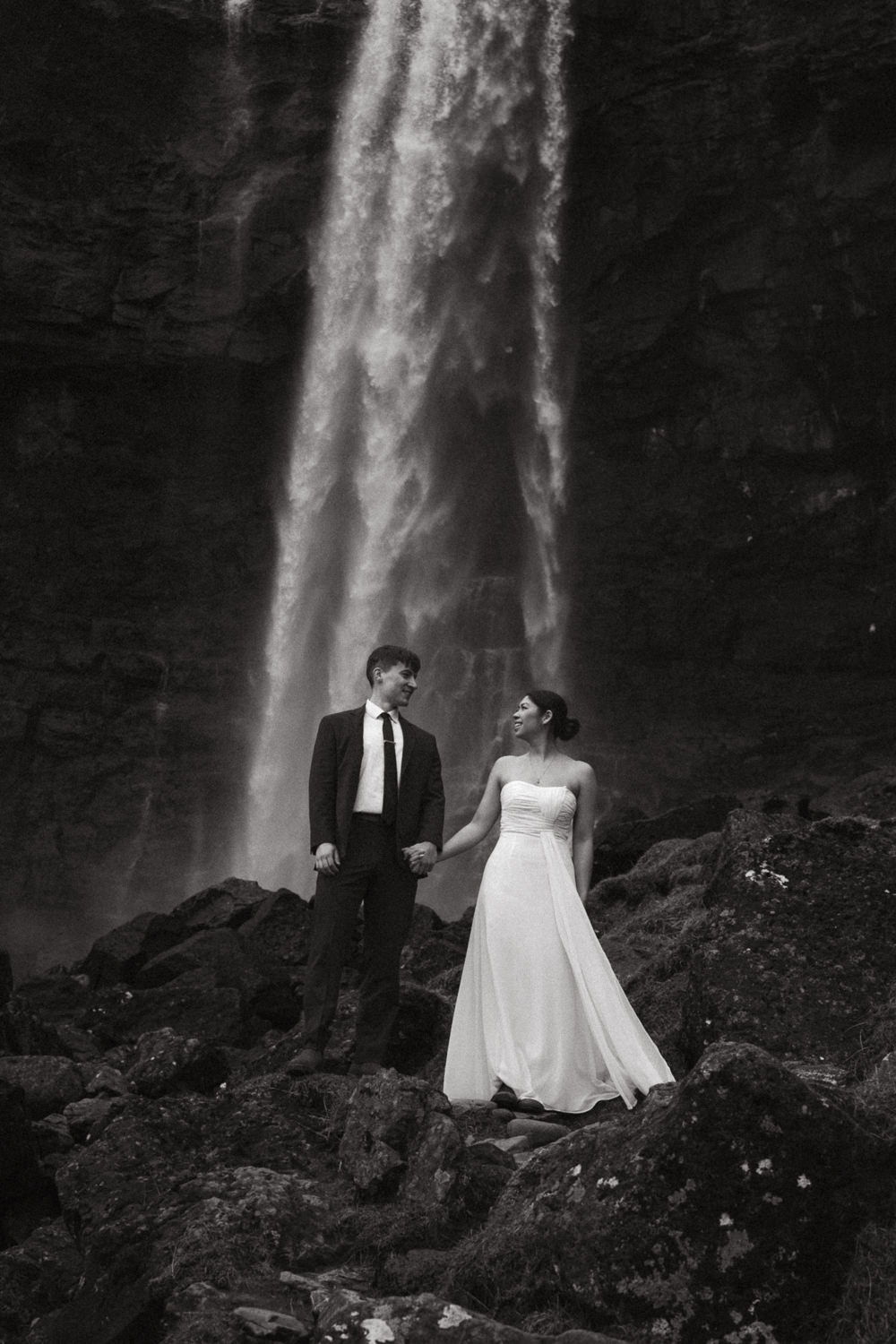 Couple eloping at Fossa Waterfall in the Faroe Islands in May, wedding dress blowing in the wind