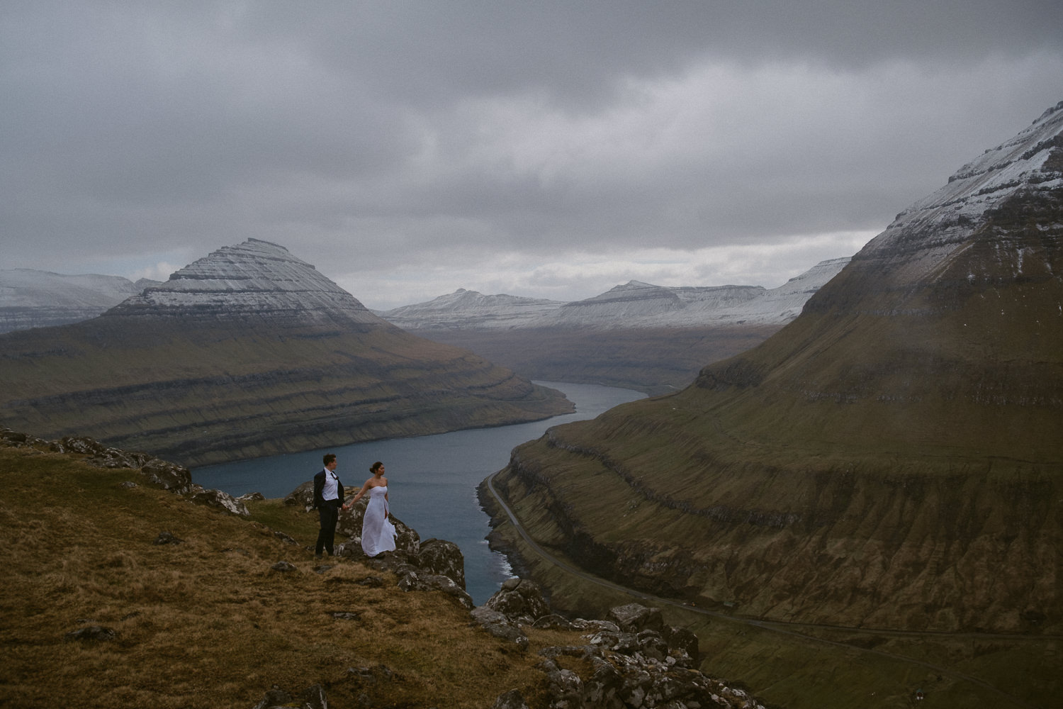 Wide-angle portrait of a bride and groom in front of a dramatic Faroe Islands landscape